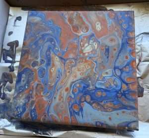 Student acrylic paint pour canvas with swirling blue and rust orange fluid art cells created at a Paint Pour Academy class