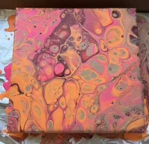 Student acrylic paint pouring canvas in warm pink, orange, and mauve tones with large rounded fluid art cells and swirling patterns
